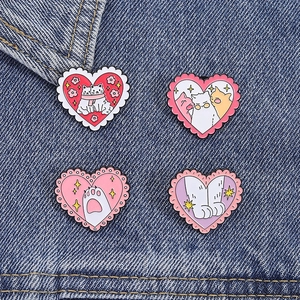 Vue détaillée de quatre pin's chat en émail en forme de cœur sur tissu denim bleu