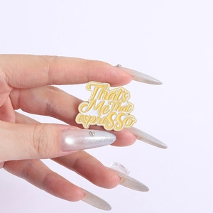Detailed shot of an enamel pin featuring That's Me That espresso lyrics in yellow and white