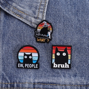 Detailed close-up of funny black cat enamel pins pinned on blue denim fabric background