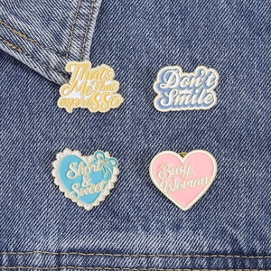 Close-up of pastel enamel pins with English slogans on dark blue denim fabric texture