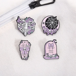 Detail of four purple enamel skull pins featuring coffin and tombstone on white canvas