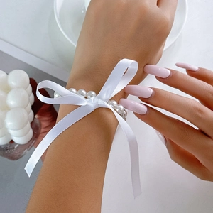 Detail van een parelarmband met een elegante witte satijnen strik om een vrouwenpols