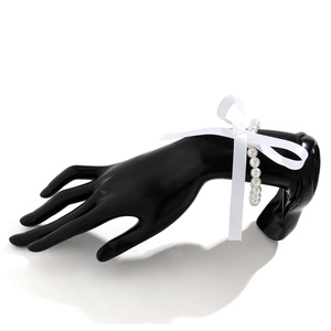 Detail van witte parelarmband met satijnen strik op een zwarte handstandaard voor sieraden