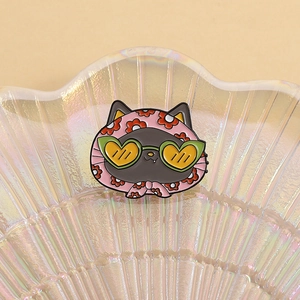 Dettaglio di una spilla in smalto a forma di gatto nero con foulard rosa e fiori
