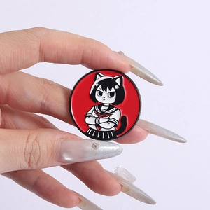 Détail d'un badge en émail rouge avec une fille chat tenu à la main sur fond gris