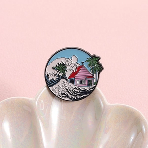 Detail of round enamel pin with ocean wave, palm trees and red house on a shell tray