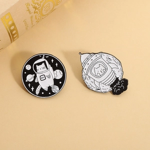 Close-up of cute cartoon cat astronaut and rocket enamel pins on textured paper