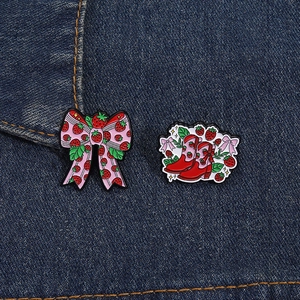 Close-up of strawberry enamel pins featuring a pink bow and red boot on denim fabric