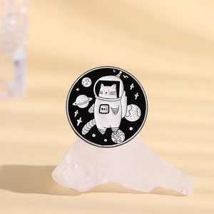 Detail of round enamel astronaut cat brooch pin with planet and comet motifs on a stone