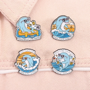 Detail of four blue dolphin enamel pins with summer themes on pink fabric texture