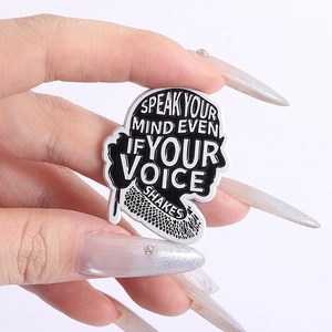 Detail showing enamel brooch with motivational text and silhouette held by fingers