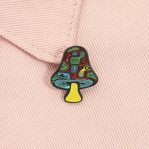 Detail of artistic mushroom enamel pin with colorful swirls on pink fabric jacket