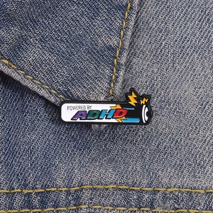 Spilla smaltata a batteria Powered by ADHD su una giacca di jeans blu