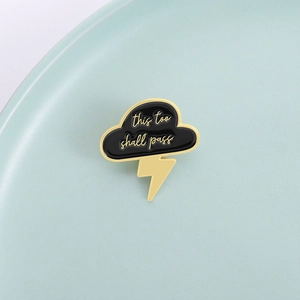 Close-up of cloud enamel pin with this too shall pass quote and golden lightning bolt detail