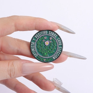 Detail of round enamel brooch featuring floral patterns and Spanish motivational text