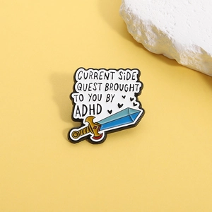 Dettaglio della spilla a spada in smalto con testo Current Side Quest e cuore ADHD