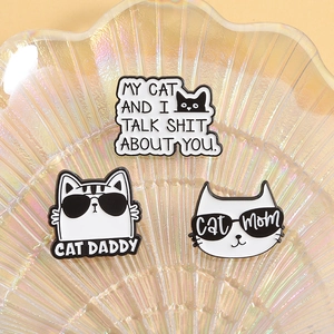 Detailed close-up of funny enamel cat brooches with witty text on a pearl shell tray