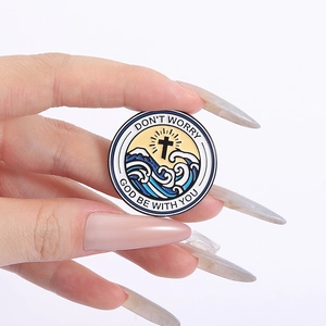 Detail of hand holding a round enamel pin with a black cross and golden sun design