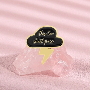 Detail of black cloud and gold lightning brooch with this too shall pass engraving