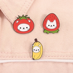 Macro d'épingles en émail de chat tomate, fraise et banane sur tissu rose tendre