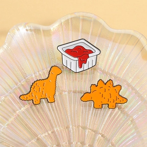 Enamel pins set featuring dinosaur chicken nuggets and tomato sauce on a shell tray
