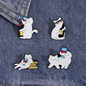 Detail view of four cat enamel pins with wine and book themes on denim fabric
