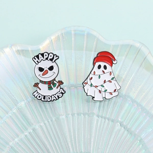 Funny Christmas snowman and festive ghost enamel pins on a pearlescent shell tray