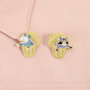 Detailed view of enamel animal pins featuring a raccoon and possum in trash cans