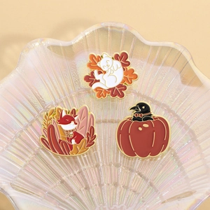 Three autumn enamel pins featuring cat with maple leaf fox and pumpkin on shell dish