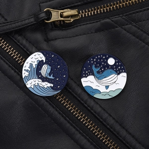 Detailed view of ocean-themed enamel pins with whale and starry sky on black leather jacket
