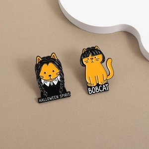 Detail of Halloween cat enamel pins featuring Wednesday Adams style and Bobcat text