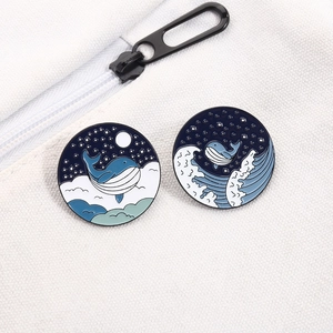 Detail of two circular enamel whale pins featuring ocean waves and starry night sky motifs