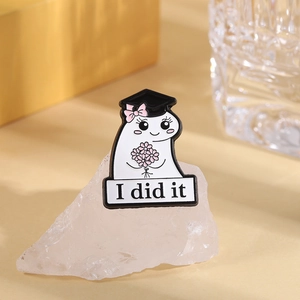 Macro view of cute cartoon ghost enamel pin with graduation cap and I Did It text