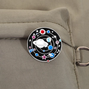 Détail d'une broche ronde en émail galaxie épinglée sur un sac à dos en toile kaki