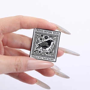 Close-up of black and white enamel crow pin with Crows Before Bros text design