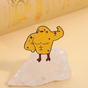 Détail du badge émaillé poussin musclé créatif posé sur une pierre blanche naturelle