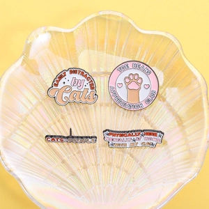 Close-up of four cute cat-themed enamel pins on a decorative shell tray with yellow background