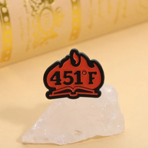 Macro d'un pin's Fahrenheit 451 en émail avec motif de flamme et livre sur pierre