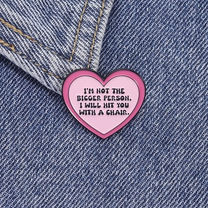 Gros plan d'un pin's en émail coeur rose avec citation amusante sur veste en jean