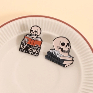 Detail of gothic enamel pins showing skull reading books on a ceramic textured plate