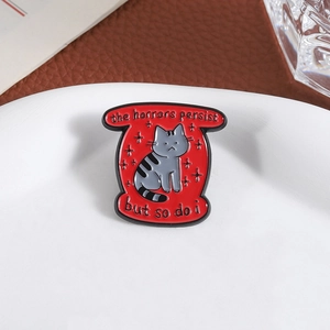 Pin's en émail chat gris sur bouclier rouge avec texte the horrors persist but so do i