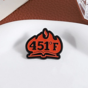 Fahrenheit 451 literary enamel pin featuring red flames and a book icon on a leather surface