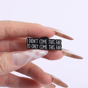 Detail of hand holding enamel pin with quote I DIDNT COME THIS FAR TO ONLY COME THIS FAR