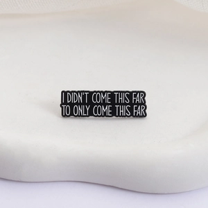 Macro view of rectangular enamel pin with motivational quote on a white decorative tray