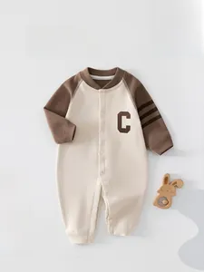 Détail d'une barboteuse pour bébé avec boutons et un écusson marron en forme de C
