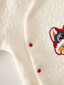 Close-up of baby quilted cotton fabric featuring snap buttons and red lion embroidery