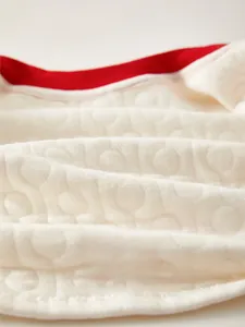 Detail of baby thermal quilted cotton fabric with beige texture and red piping trim