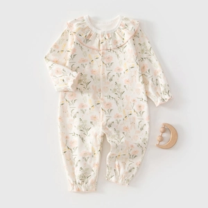 Detail of floral baby romper with ruffled collar and wooden moon rattle on gray backdrop