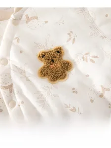 Détail de barboteuse bébé avec broderie ours en peluche 3D et motif de forêt de Noël