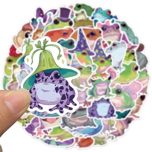 Close-up of a hand holding a waterproof purple cartoon frog sticker for DIY luggage